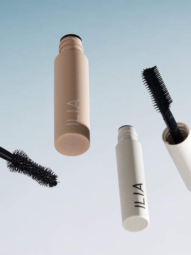 Floating ILIA mascaras and wands against a soft blue gradient.