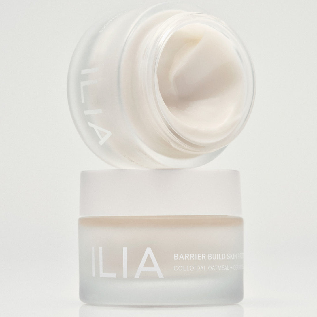 ILIA's Barrier Build Moisturizer open on it's side on top of another Barrier Build jar on a light background.
