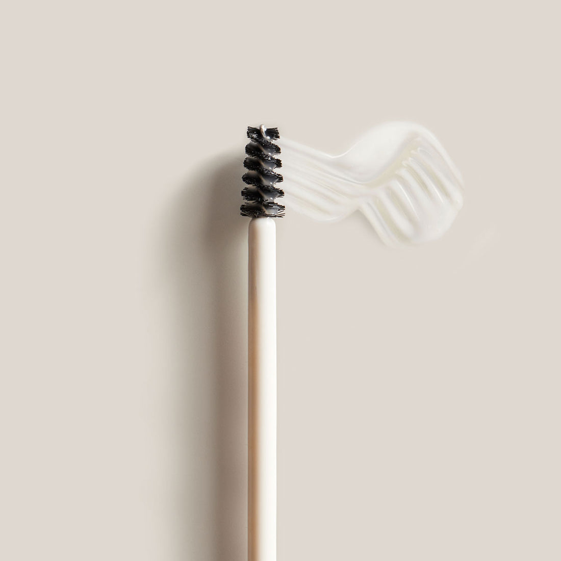 The brow gel applicator with a swatch of the gel next to it on a light background.