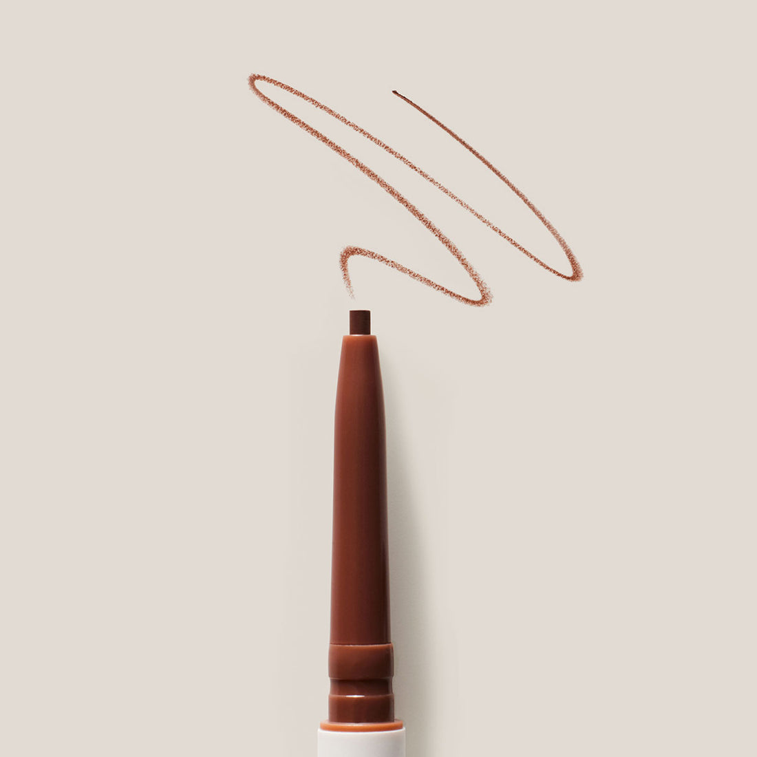 A close up of ILIA's Brow Pencil with a swatch of the shade on a light background.