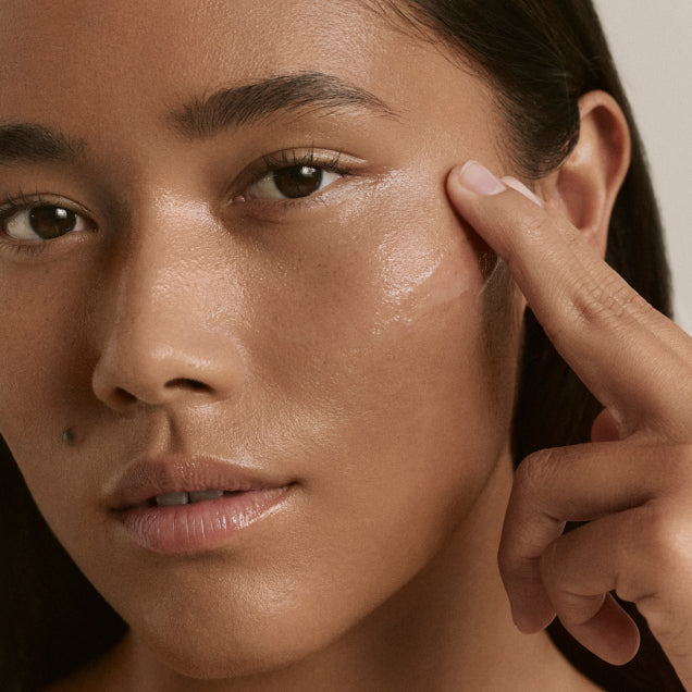 A model using two fingers to apply ILIA's Base Face Milk to their face.