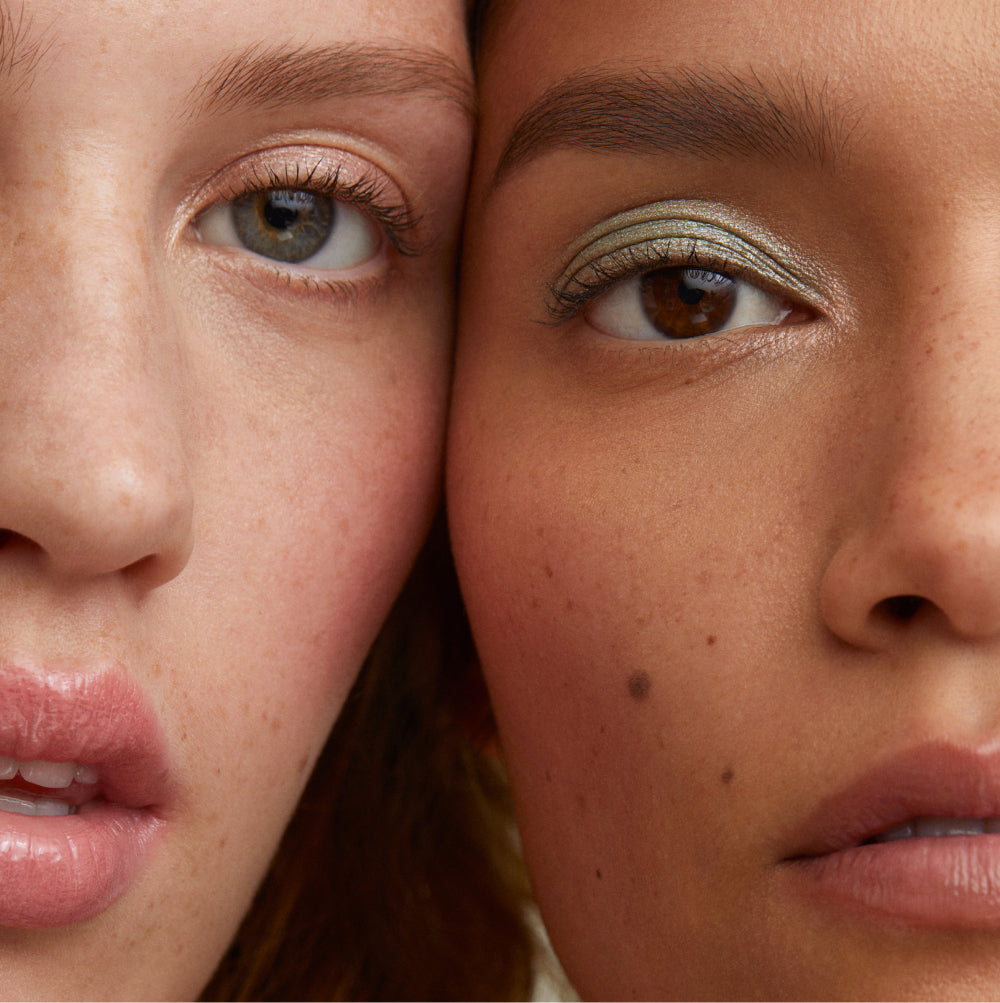 Two models with their faces close together, showcasing shimmery pink and green eyeshadow looks.