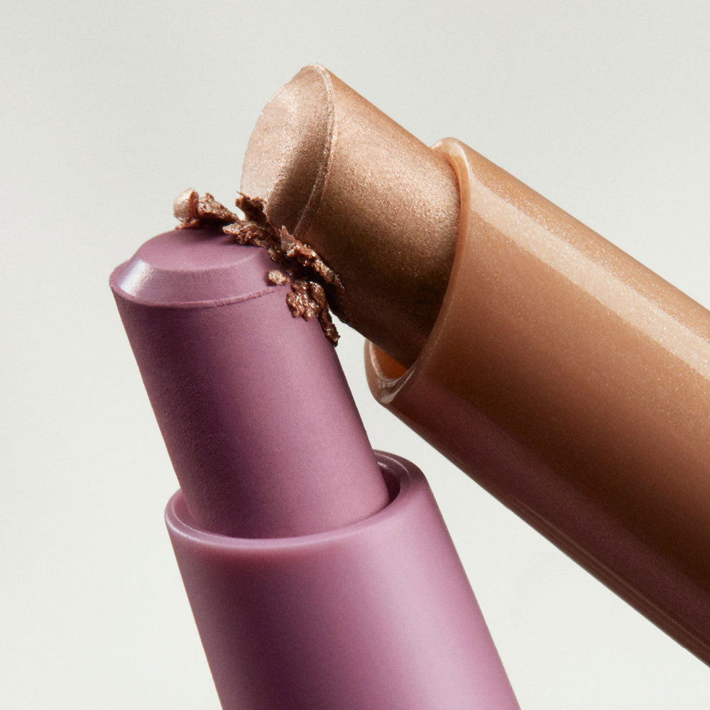 Close-up of two cream eyeshadow sticks in shimmer bronze and matte lilac pink, with product crushed at the tips.