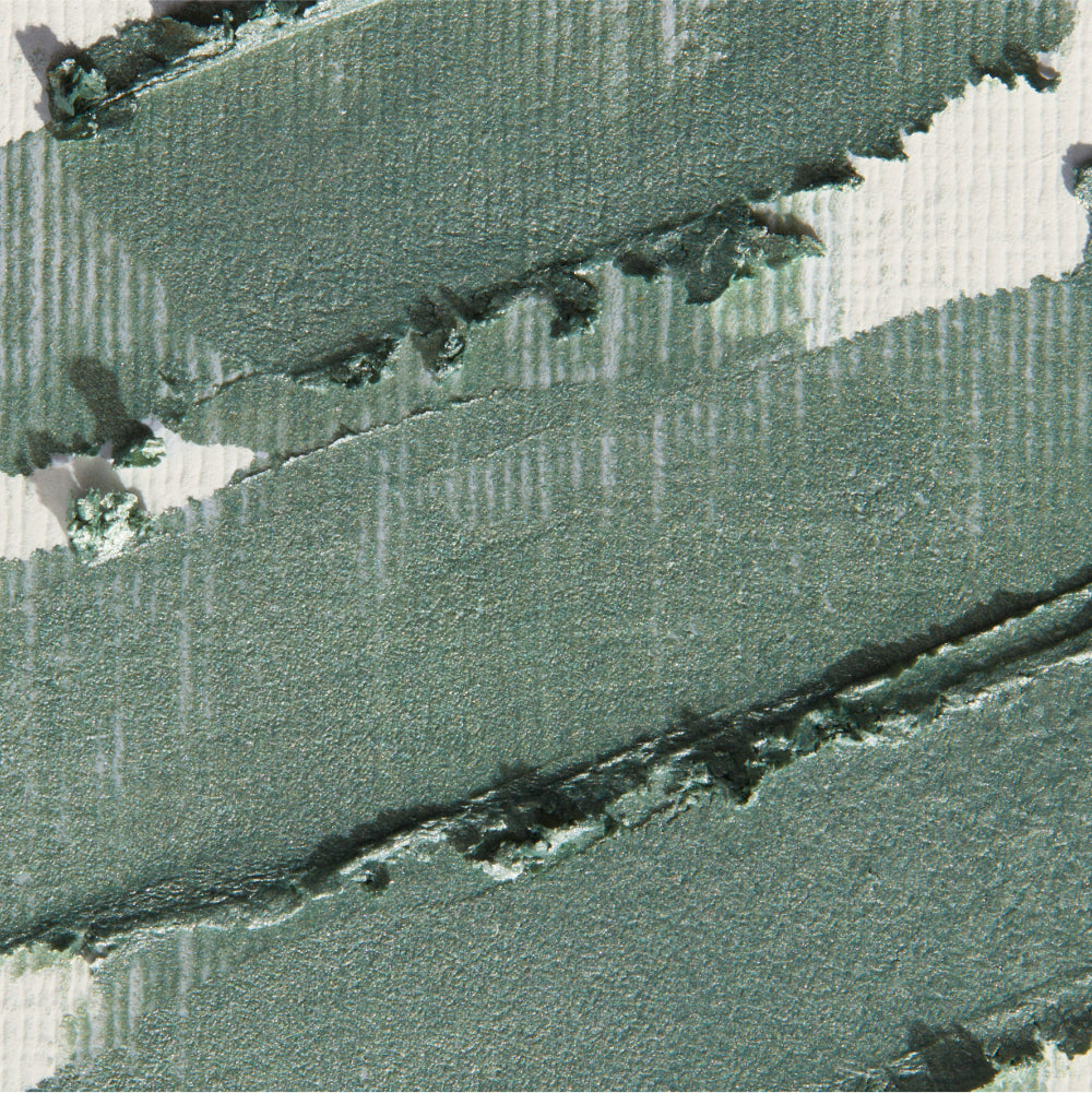 Smudged swatches of seafoam green shimmer cream eyeshadow on a textured white surface.