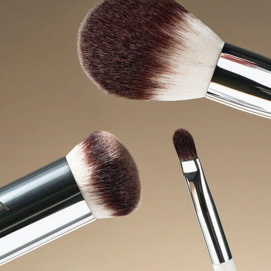 Three assorted ILIA brushes set against a soft tan gradient.