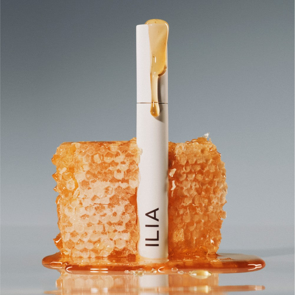 Limitless Lash Mascara with honey dripping down the container while surrounded by honeycomb on a light grey background.