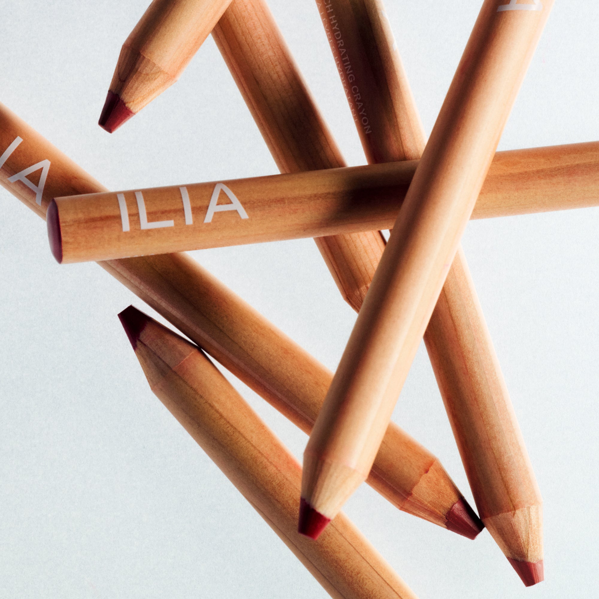 ILIA lip pencils arranged in a scattered formation on a light gray background.